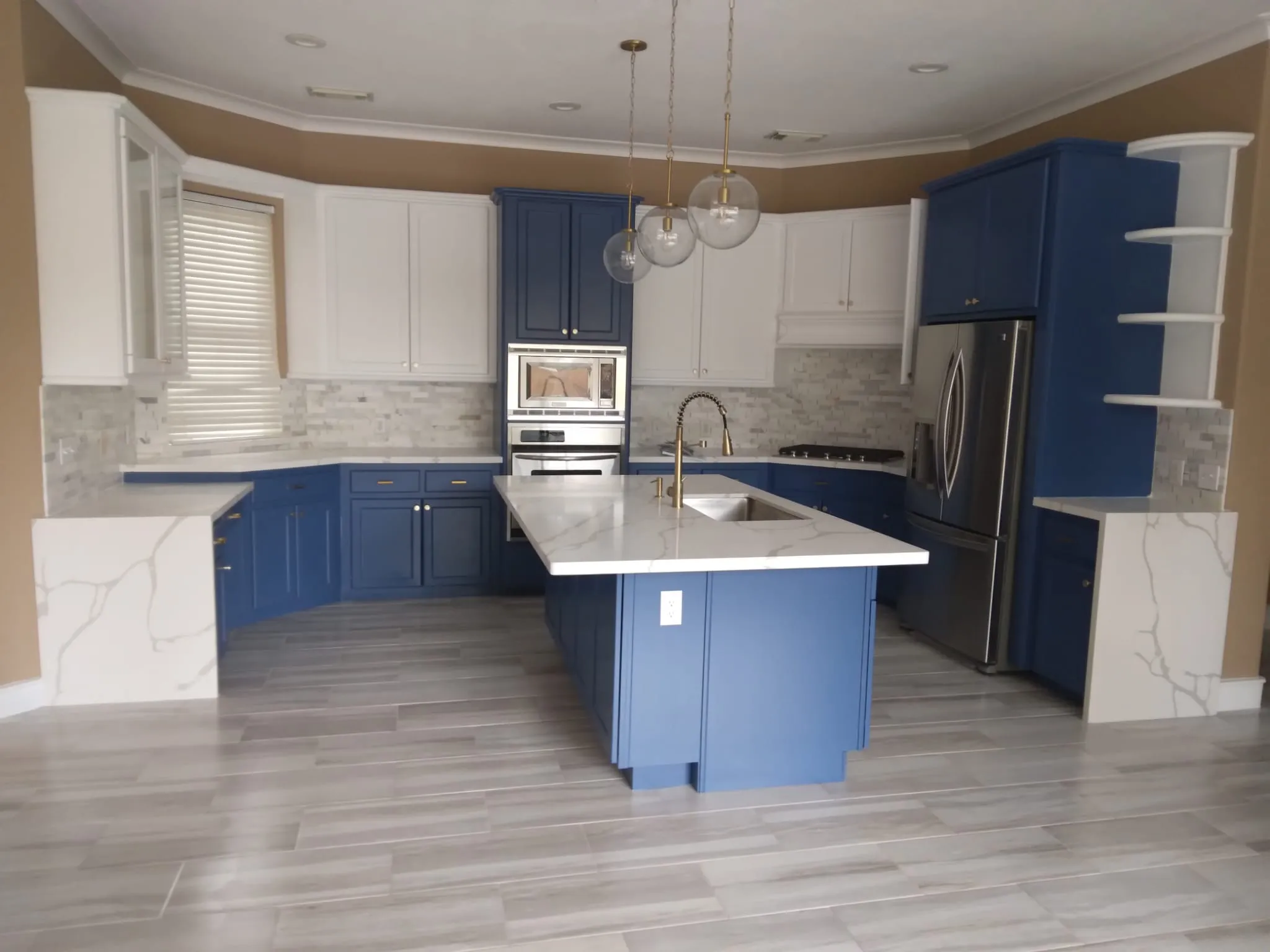 Modern kitchen with blue lower cabinets, white upper cabinets, marble countertops, and stainless steel appliances.