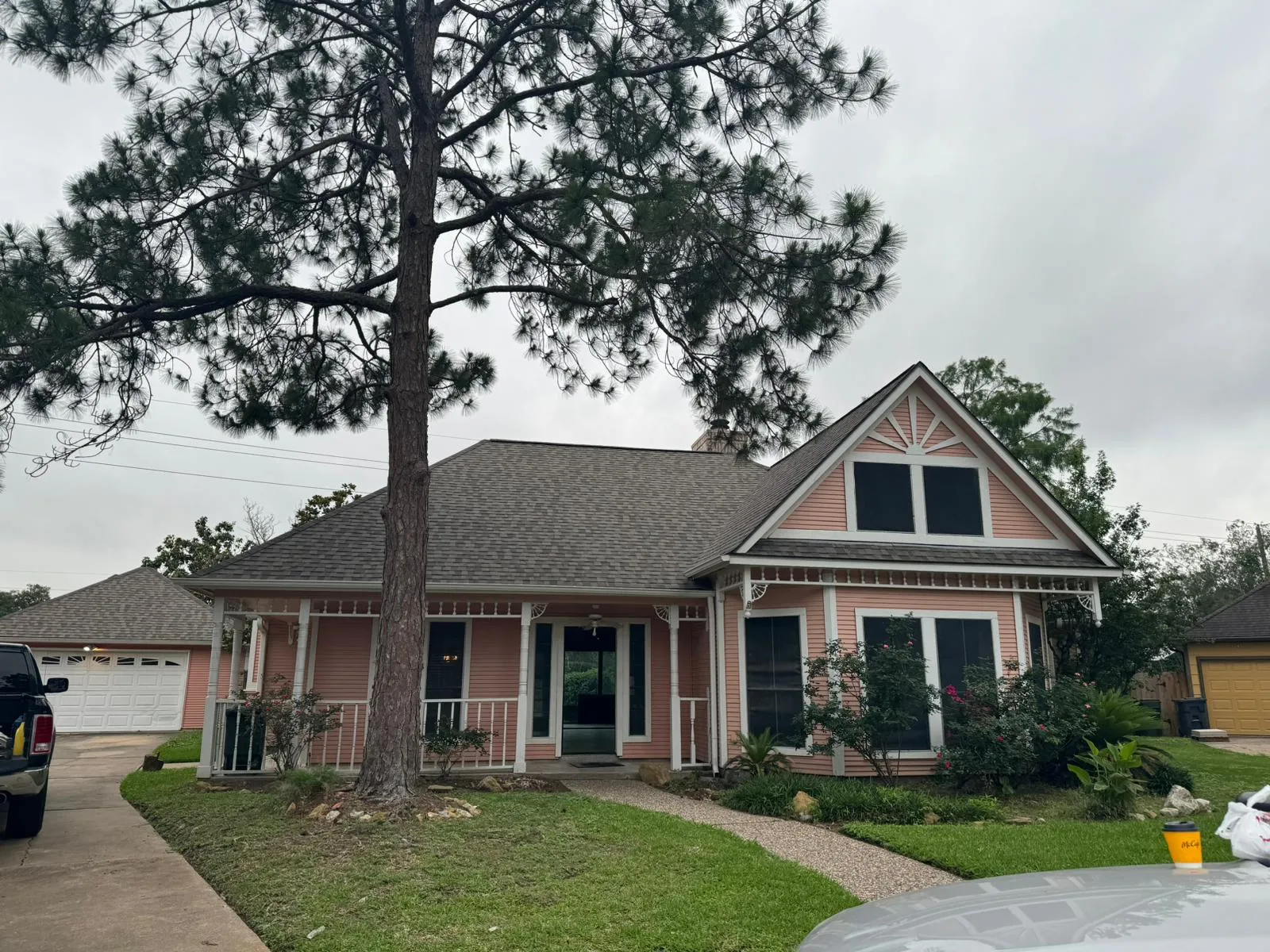 Pink single-story house with white trim, a front porch, and a large tree in the yard on a cloudy day.
