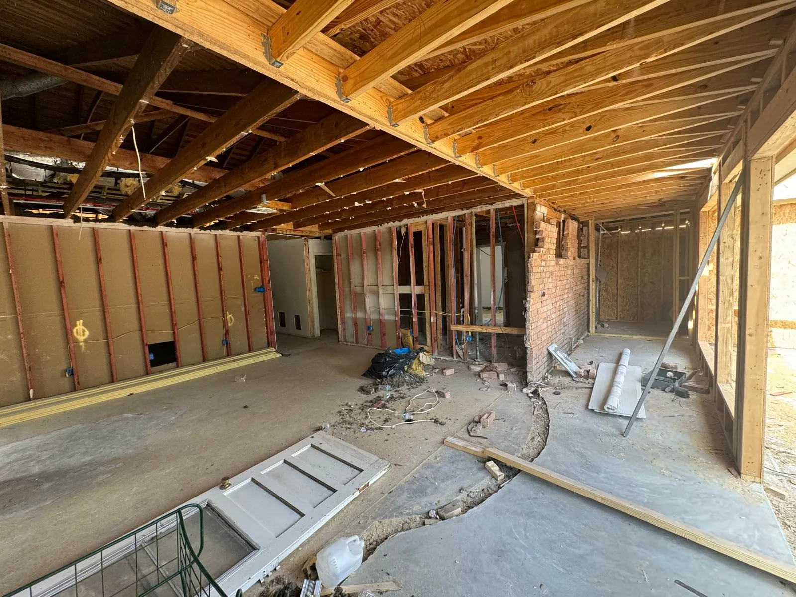 Interior of a house under renovation showing exposed wooden ceiling beams, partially framed walls, and a concrete floor with a trench cut for foundation work.