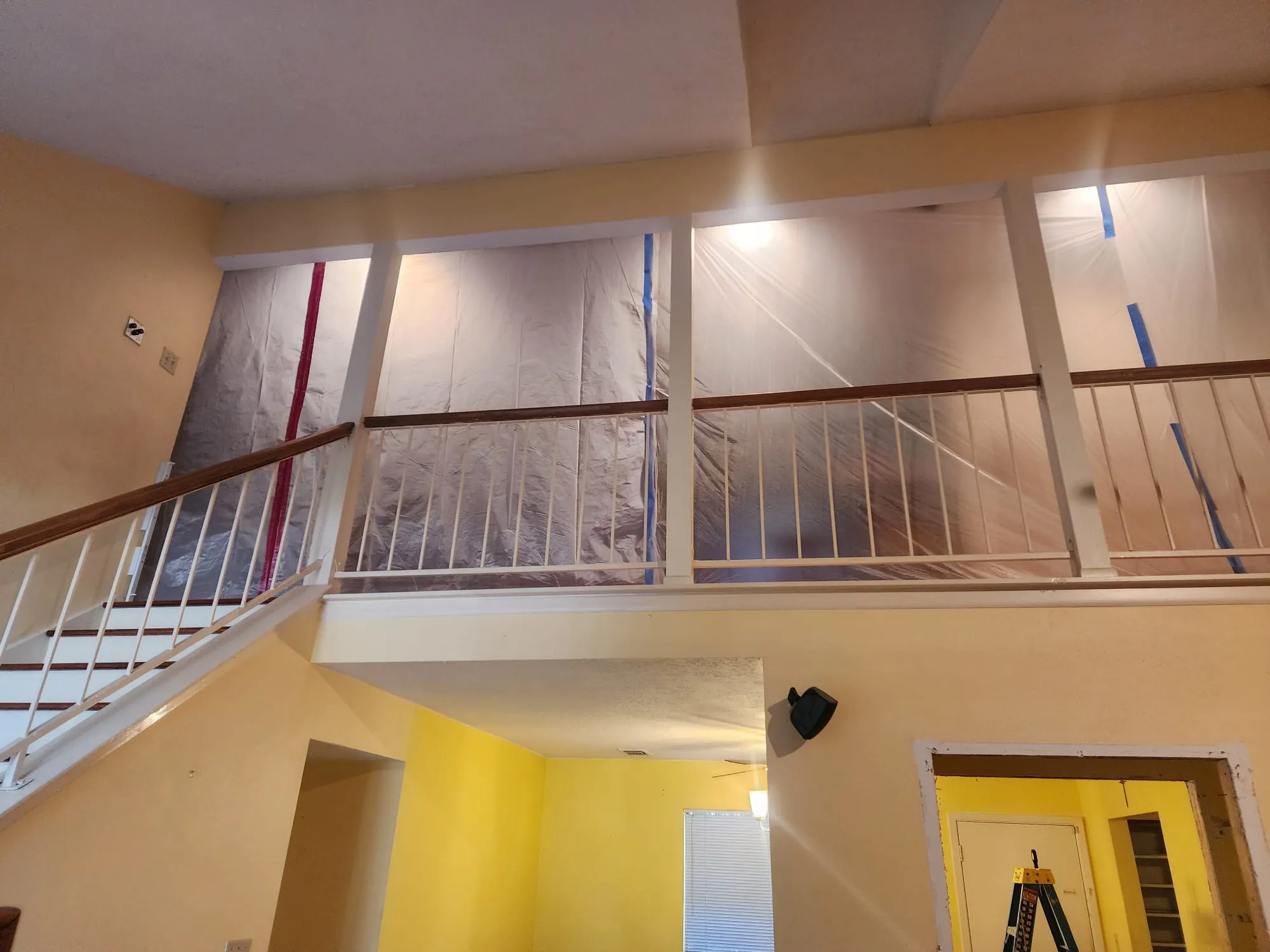 Interior view of a house with a staircase and upper railing covered in protective plastic sheeting for remodeling.
