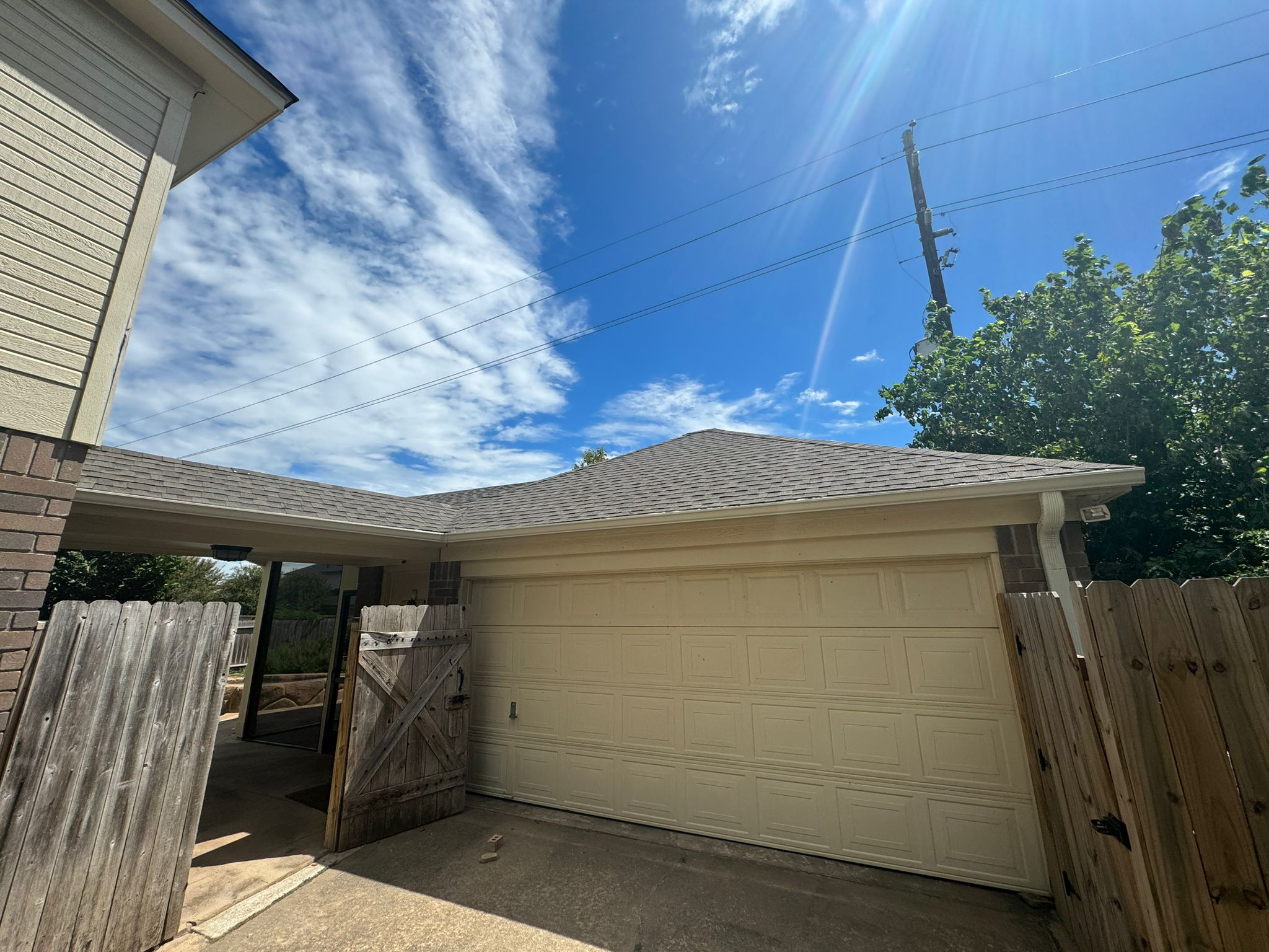 Closed beige garage door with an open wooden gate in front, under a partly cloudy blue sky.