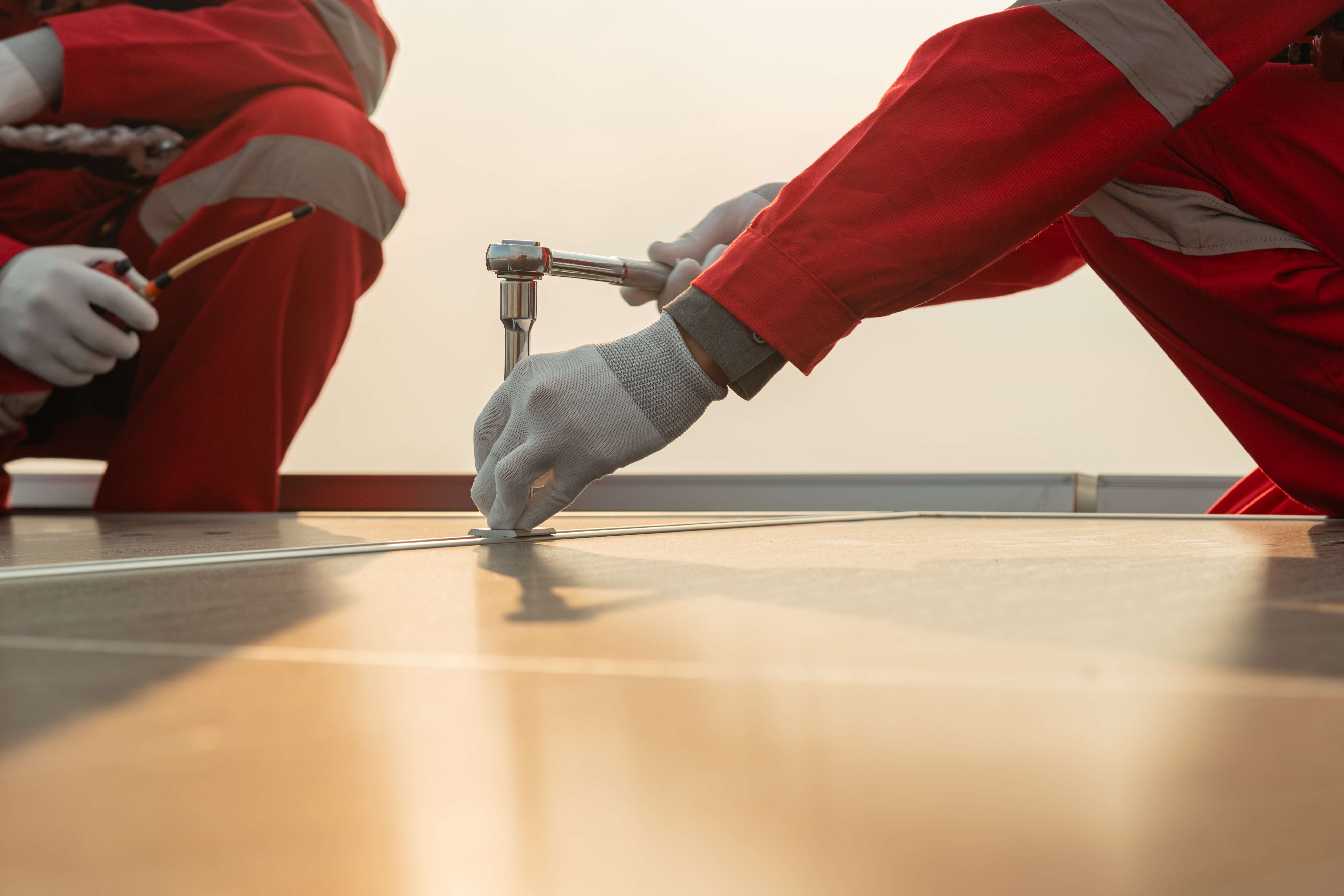Technician in red protective clothing and gloves tightening a bolt with a ratchet wrench.
