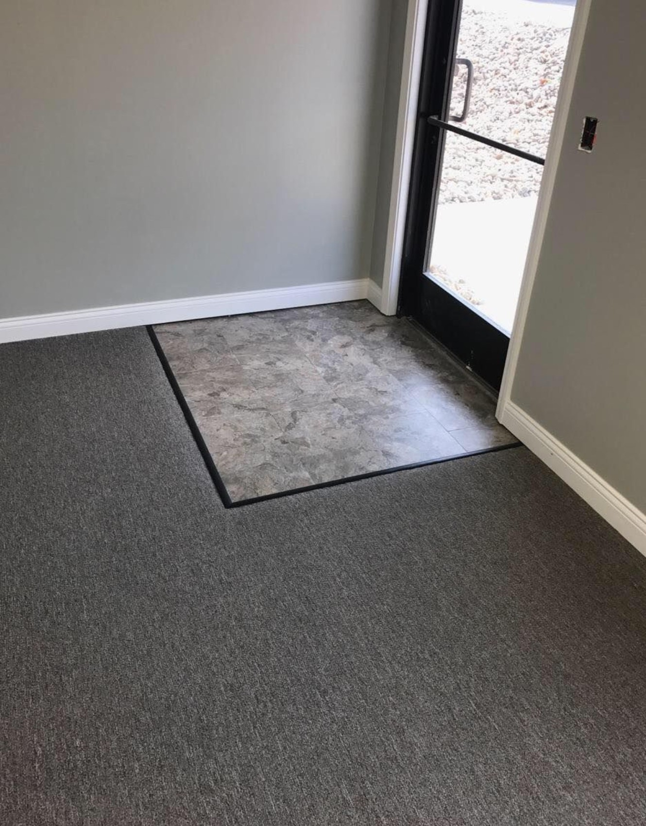 Entryway with gray carpet flooring and a small section of gray tile flooring near a glass door.