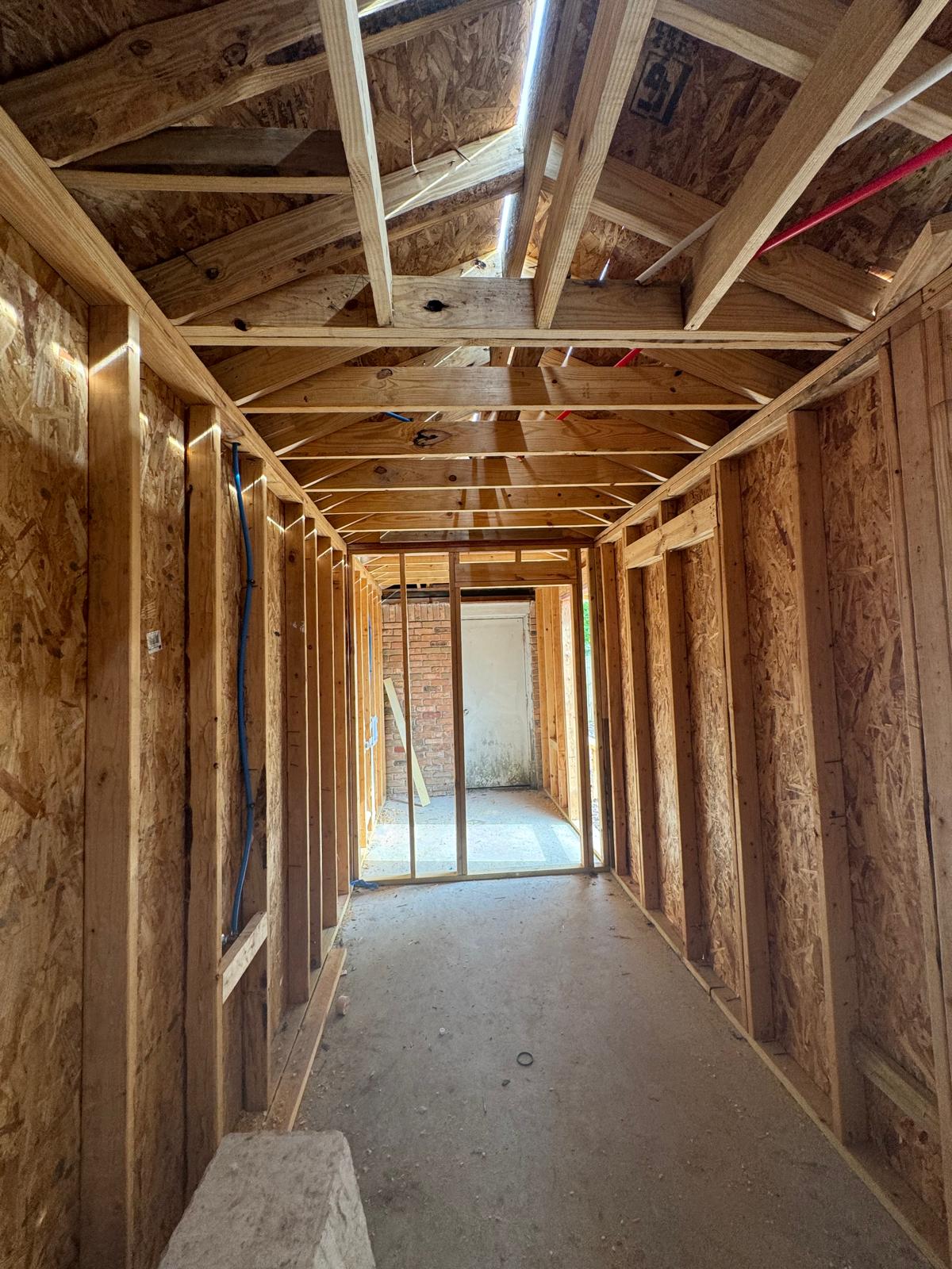 Interior view of a wooden frame structure under construction with exposed beams and plywood walls.