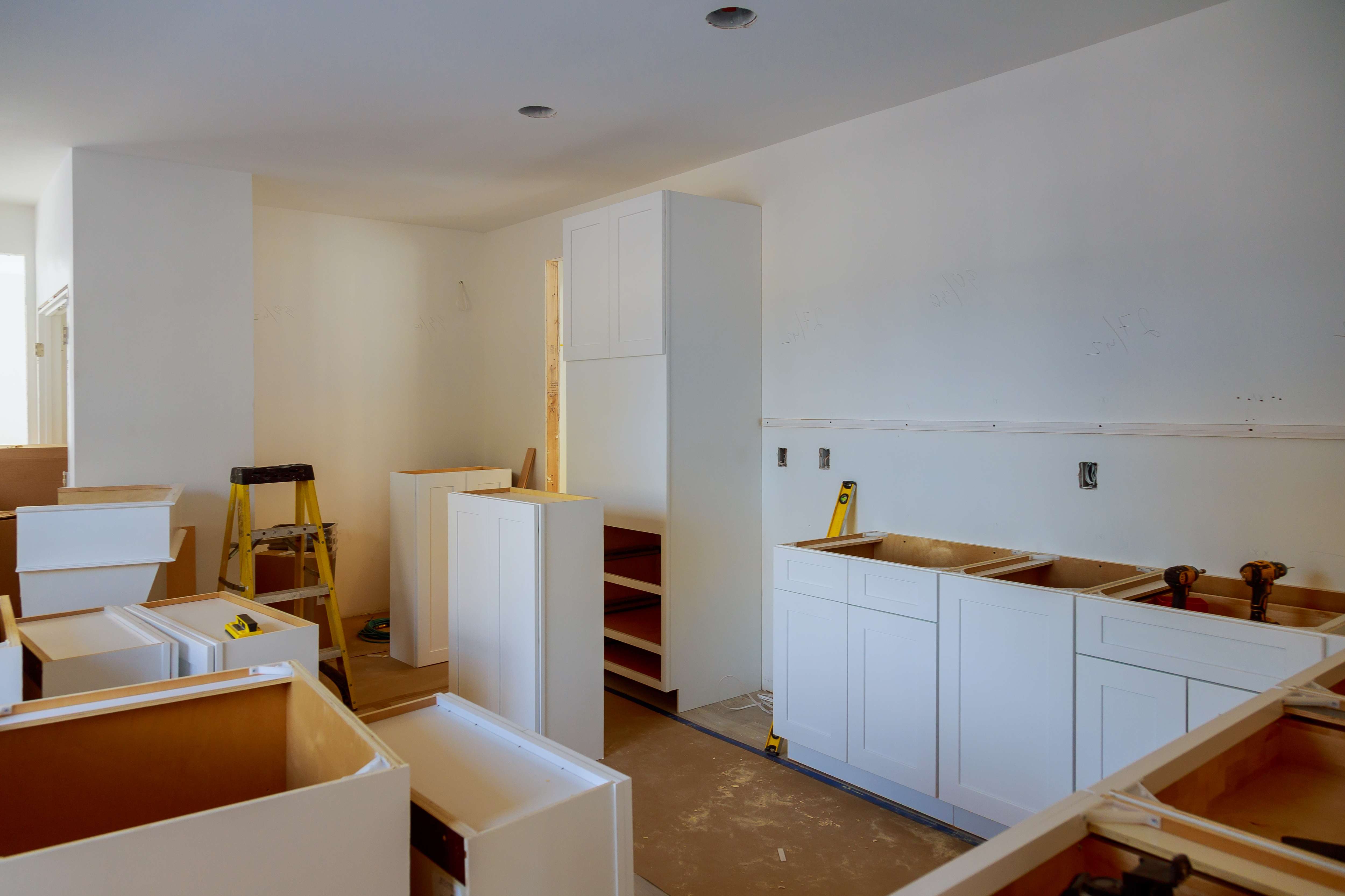 Interior view of a kitchen under renovation with white cabinets partially installed and tools scattered around.