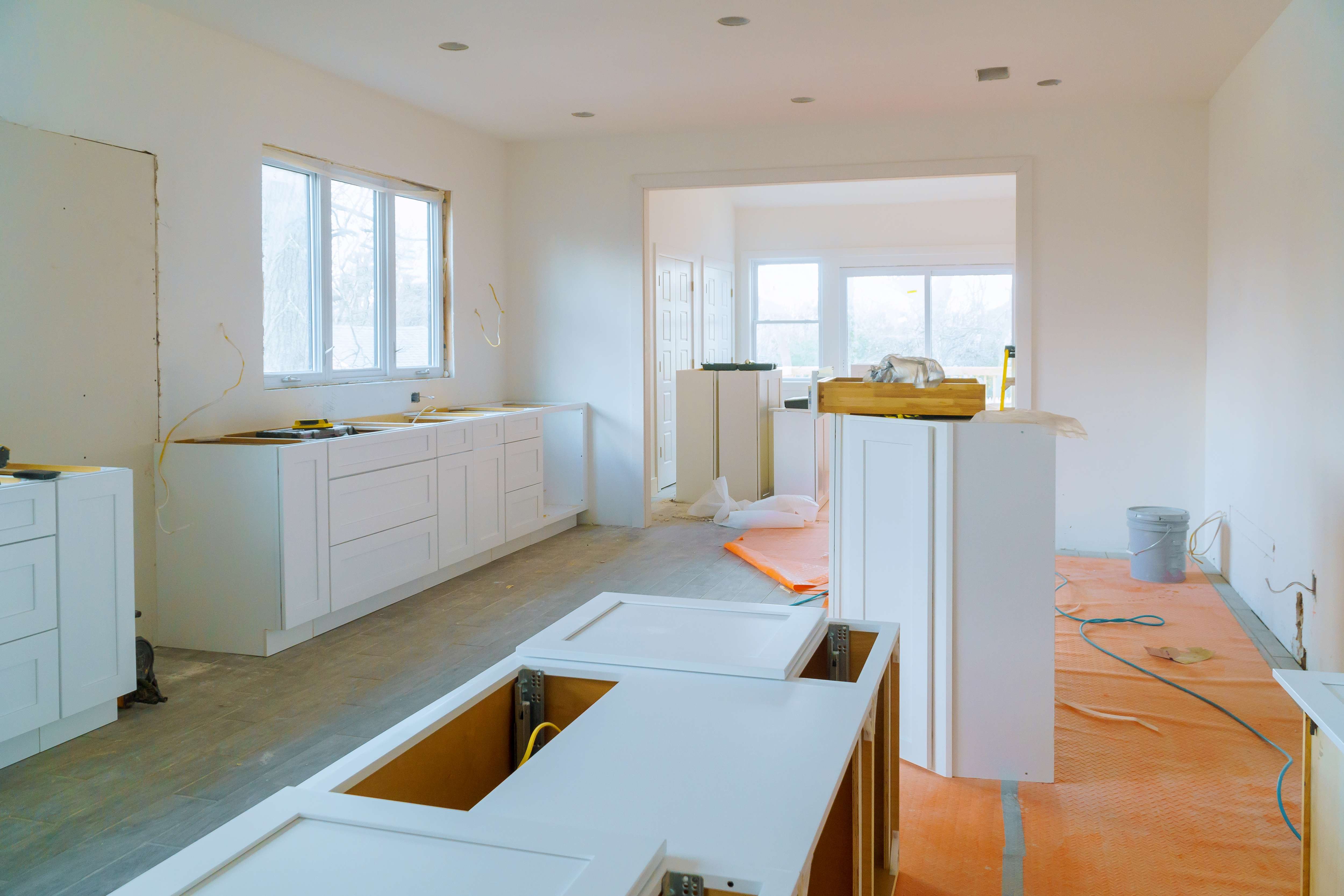 Interior of a kitchen under renovation with white cabinets partially installed and orange protective floor covering.