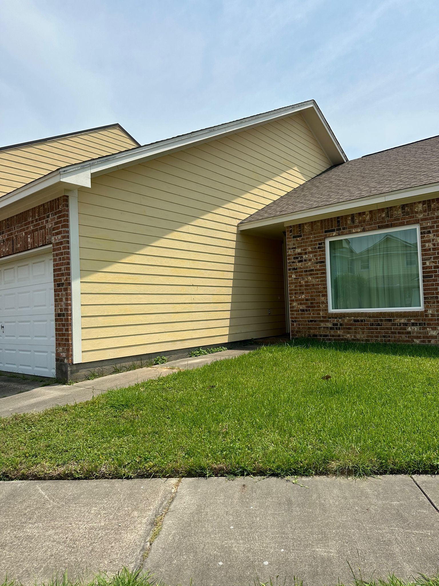 Exterior view of a suburban house with yellow siding, a white garage door, brick walls, and a green grassy front yard.