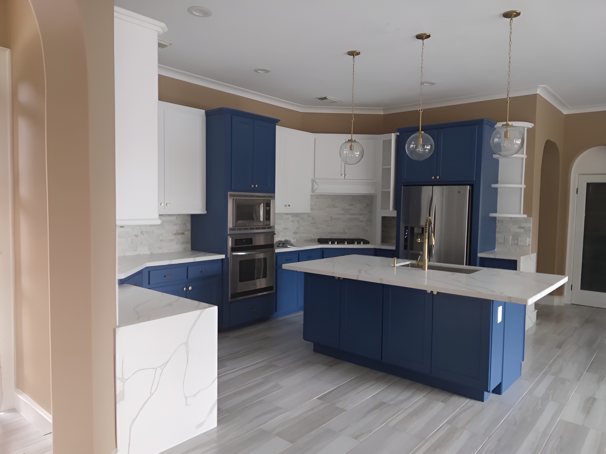 Modern kitchen with blue lower cabinets and island, white upper cabinets, marble countertops, stainless steel appliances, and three pendant lights.