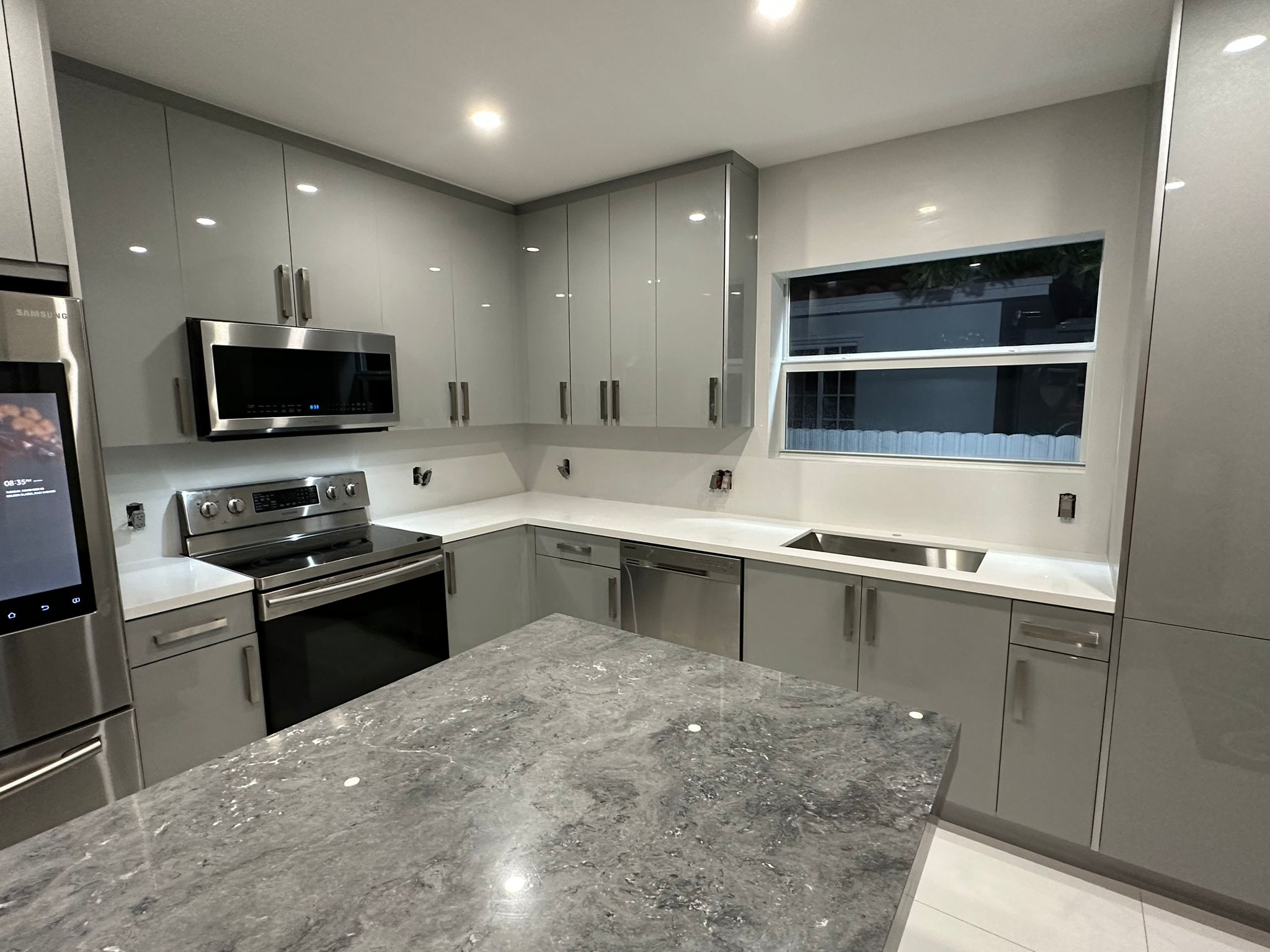 Modern kitchen with gray cabinets, stainless steel oven, microwave, dishwasher, refrigerator, and a gray marble island countertop.