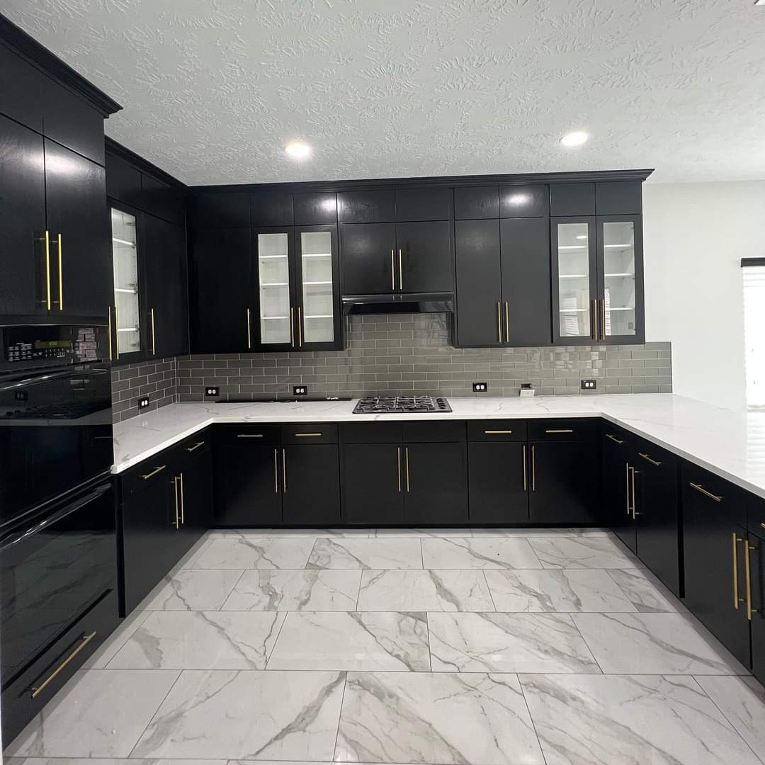 Modern kitchen with black cabinets, gold handles, gray subway tile backsplash, white marble countertops, and marble tile floor.