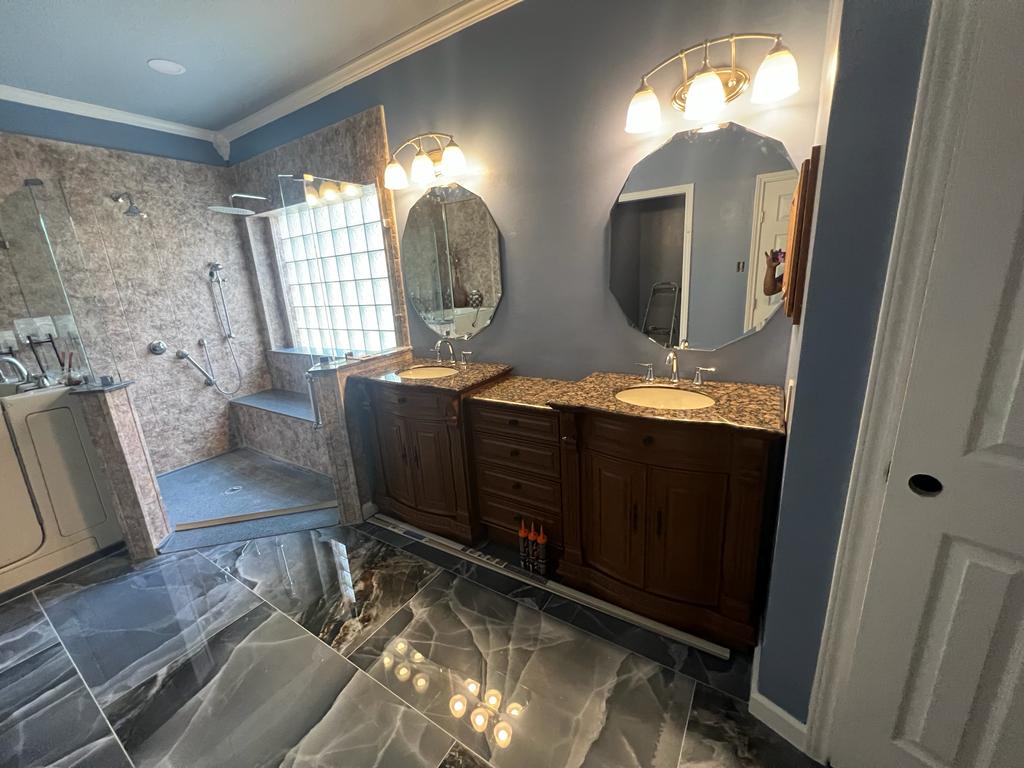 Modern bathroom with dual wooden vanities, granite countertops, octagonal mirrors, and walk-in glass shower with built-in bench.