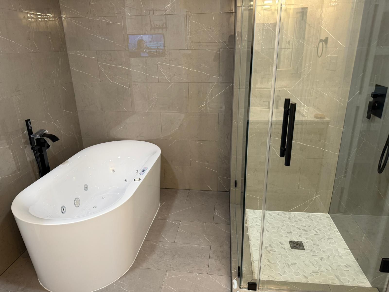 Modern bathroom featuring a white freestanding bathtub with black faucet and a glass-enclosed shower with hexagonal tiled floor.