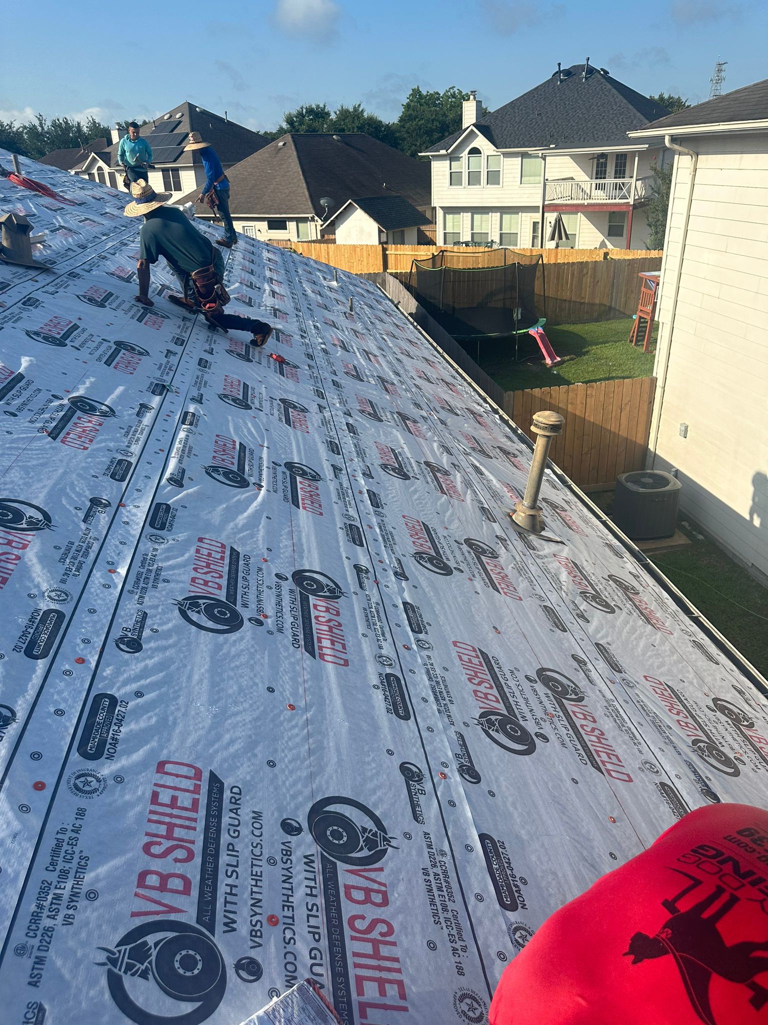 Roofers installing VB Shield roofing underlayment on a residential roof under clear sky.