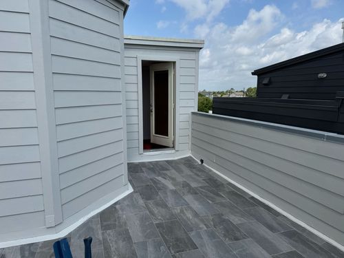 Small outdoor balcony with gray tiled flooring, light gray siding walls, and a door leading inside.