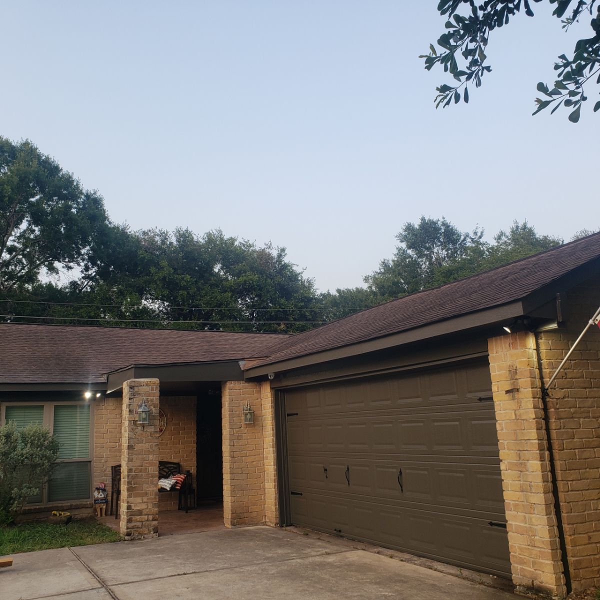 Single-story brick house with a dark brown garage door, covered porch, and trees in the background.
